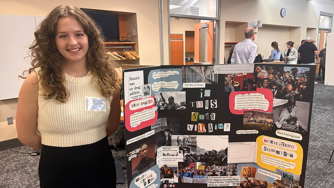 student stands in front of their poster